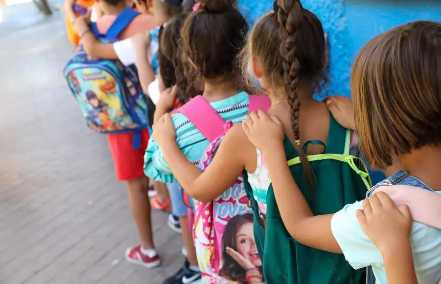 Varios ni&ntilde;os hacen fila con sus mochilas